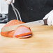 A person using a Victorinox carving knife to slice a ham on a counter.