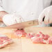 A person in white gloves using a Mercer Culinary Z&#252;M&#174; Forged Carving Knife to cut meat on a cutting board.