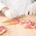 A person in white gloves using a Mercer Culinary Z&#252;M&#174; Forged Carving Knife to cut meat on a wooden cutting board.