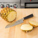 A Mercer Culinary Z&#252;M Santoku knife next to a pineapple cut in half on a cutting board.