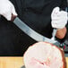 A person in a chef's uniform using a Victorinox cimeter knife to cut meat.