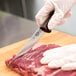 A person in a glove using a Victorinox boning knife to cut meat on a counter.