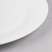 A close-up of a white Reserve by Libbey International bone china dinner plate with a curved edge and a white rim.