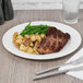 A Reserve by Libbey International bone china dinner plate with meat, potatoes, and green beans with a fork and knife on a white napkin.