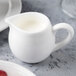 A white Reserve by Libbey bone china creamer with a handle on a table full of milk.