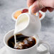 A person pouring milk into a cup of coffee using a Reserve by Libbey bone china creamer.