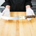 A person in white gloves holding a Victorinox Cimeter knife with a rosewood handle on a wooden cutting board.