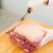 A person in gloves using a Victorinox curved breaking knife to cut meat.