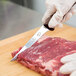 A person in gloves using a Victorinox narrow stiff boning knife to cut meat on a cutting board.