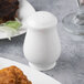 A white bone china pepper shaker next to a plate of food.