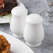 Two Reserve by Libbey bone china pepper shakers on a table with a plate of fried chicken.