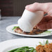 A hand holding a Reserve by Libbey bone china salt shaker over a plate of food.