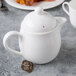 A white Reserve by Libbey bone china teapot with a lid and a tea bag on it.