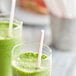 Two glasses with green smoothies and red and white striped straws.