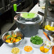 A Matfer Bourgeat 2.5 gallon salad spinner filled with green leaves, oranges, and carrots.