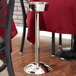 A silver metal pole with a Vollrath stainless steel wine bucket stand on a table with a red tablecloth.