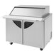 A Turbo Air stainless steel refrigerated sandwich prep table with sliding lids over food.