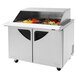 A Turbo Air stainless steel refrigerated sandwich prep table with sliding lids on a counter with food.