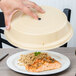 A hand holding a Cambro beige low profile plate cover over a plate of food with meat and rice.