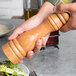 A person holding a Fletchers' Mill cherry wooden pepper mill over a salad.
