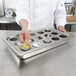 A chef holding a Vollrath 15 hole plate for egg poaching on a counter.