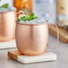 Two Acopa copper Moscow Mule mugs with ice and lime on a marble coaster.