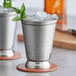 Two Acopa stainless steel mint julep cups filled with ice and mint leaves on a coaster.
