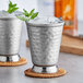 Two Acopa hammered stainless steel mint julep cups filled with ice and mint leaves.