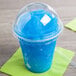 A clear plastic dome lid with a blue straw in a plastic cup with a blue slushy.