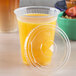A Fabri-Kal clear plastic lid on a plastic cup with a yellow drink in it.