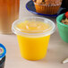 A plastic cup with a Fabri-Kal clear plastic lid and a yellow liquid with a muffin on a table.