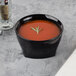 A bowl of tomato soup in a Cambro insulated bowl with a sprig of rosemary.