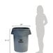 A woman standing next to a Rubbermaid Brute 44 gallon grey trash can.