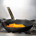 A Vollrath carbon steel fry pan with food in it on a stove.