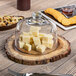 A Tablecraft Acacia round serving board with cubed cheese, crackers, and a bowl of pasta.
