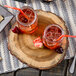 Two glasses of ice tea with straws and cherries on a Tablecraft acacia wood serving board.