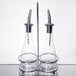 A Tablecraft Siena oil and vinegar cruet set with two glass bottles on a silver stand with metal accents.