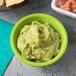A green Tablecraft ramekin filled with guacamole on a table with salsa.