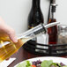 A person pouring oil into a Tablecraft Siena oil and vinegar bottle on a table with a plate of salad.