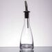 A clear glass Tablecraft Siena oil and vinegar bottle with a stainless steel spout.