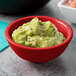 A red round ribbed melamine ramekin filled with guacamole on a table.