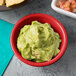 A red Tablecraft ramekin filled with guacamole on a table with salsa and chips.