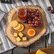A Tablecraft acacia wood serving board with crackers, cheese, and jam on it.