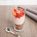 A GET Revo plastic dessert glass filled with yogurt and strawberries with a spoon.