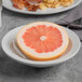 A Libbey bright white porcelain grapefruit bowl with half a grapefruit on a table in a breakfast diner.