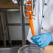 A person in a blue uniform using a Tellier manual carrot peeler on a carrot.