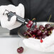 A gloved hand uses a Tellier Manual Olive/Cherry Pitter to pit a cherry.