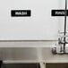 A sink with a Vollrath Traex wash sign and rinse sign on the wall above it.