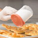 A gloved hand using a Cambro rose shaker lid to sprinkle salt on bread.