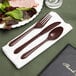 A napkin with a Hoffmaster earthtone linen-like white napkin and brown plastic fork, spoon, and knife set.